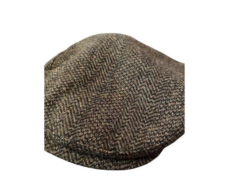 May include: A flat cap featuring a brown and black herringbone pattern. The cap has a rounded crown and a short, stiff brim at the front. The fabric displays a textured, woven appearance with a consistent zigzag design throughout the entire surface.