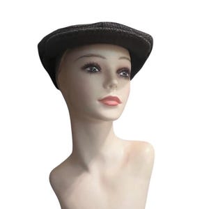 May include: A dark gray and black herringbone patterned flat cap made of a textured wool-like fabric. The cap features a rounded crown and a short, stiff brim that extends over the forehead, providing a classic silhouette and structured shape.