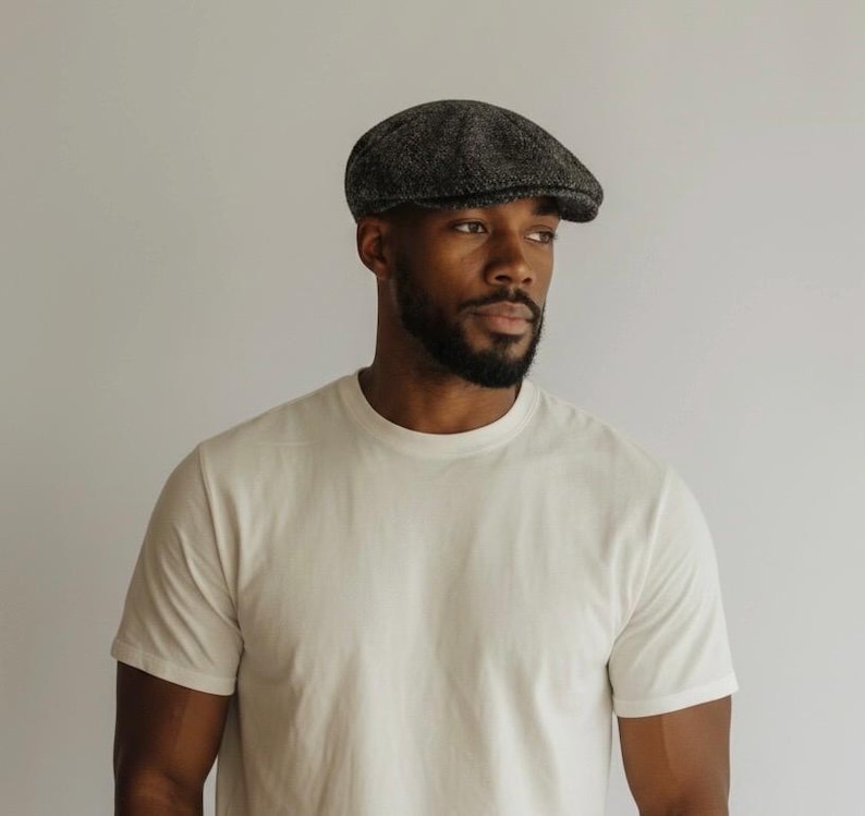 May include: A charcoal grey and black speckled flat cap with a rounded crown and a short, stiff brim. The cap features a textured, woven fabric construction with a classic panel design that sits low on the head, providing a structured silhouette.