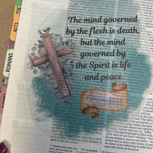 Könnte beinhalten: Eine Bibelseite mit dem Text „Der Geist, der vom Fleisch beherrscht wird, ist der Tod, aber der Geist, der vom Geist beherrscht wird, ist Leben und Frieden.“ Ein Holzkreuz und Aquarell-Akzente überlagern den Text.