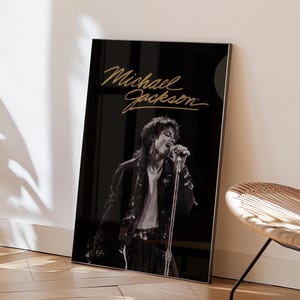 Puede incluir: Una impresión de arte mural rectangular enmarcada que presenta una fotografía en blanco y negro de Michael Jackson cantando en un micrófono. El nombre Michael Jackson está escrito en cursiva dorada en la parte superior sobre un fondo negro.