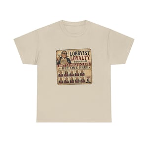 May include: A beige t-shirt with a graphic that reads "Lobbyist Loyalty Program." The graphic features an illustration of a man holding a drink and a cigar, and images of politicians.