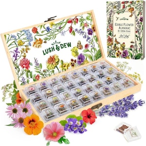 Puede incluir: Una caja de madera con un diseño floral y el texto "Lush & Dew" contiene pequeños recipientes transparentes llenos de varias flores secas. Un libro "Edible Flower Almanac" es visible. Flores frescas, incluyendo lavanda e hibisco, están dispuestas alrededor de la caja.
