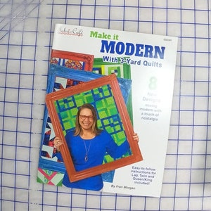 May include: A book cover with a woman holding a framed quilt. The book is titled "Make it MODERN with 3-Yard Quilts" and features 8 new designs mixing modern with a touch of nostalgia. Easy-to-follow instructions for lap, twin, and queen/king quilts are included. The book is by Fran Morgan.