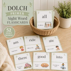 May include: A set of 52 Dolch Primer sight word flashcards featuring educational text and illustrations. The cards are printed on white paper with sage green accents, displayed in a woven basket and spread out on a wooden surface.