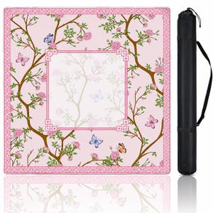 May include: A square, light pink mat featuring a floral pattern with brown branches, pink blossoms, and colorful butterflies, framed by a geometric border. A black cylindrical carrying case with an adjustable shoulder strap is positioned to the right.