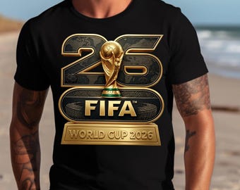 Op de afbeelding: Zwart T-shirt met een goudkleurig FIFA World Cup 2026-ontwerp. Het ontwerp bevat het nummer 26, een trofee, het FIFA-logo en de tekst "World Cup 2026". Het shirt wordt door een persoon gedragen.
