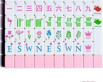 Puede incluir: Un juego de fichas de mahjong blancas con reverso rosa, con diseños coloridos de flores, bambú, dragones y direcciones. Las fichas incluyen palos numerados, comodines con coronas rosas y letras de dirección. Incluye dados de color rosa.