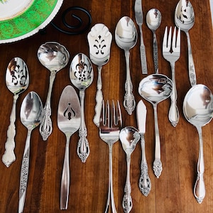 May include: A set of 16 silver-plated serving utensils with ornate handles. The utensils include spoons, forks, a knife, and serving spoons.