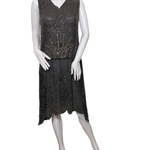 May include: A sleeveless black beaded dress with a sunburst design in the center of the bodice. The dress has a V-neck and a high waist.