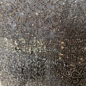 May include: A close-up of a black fabric with silver beading and sequins. The fabric has a delicate, intricate pattern.