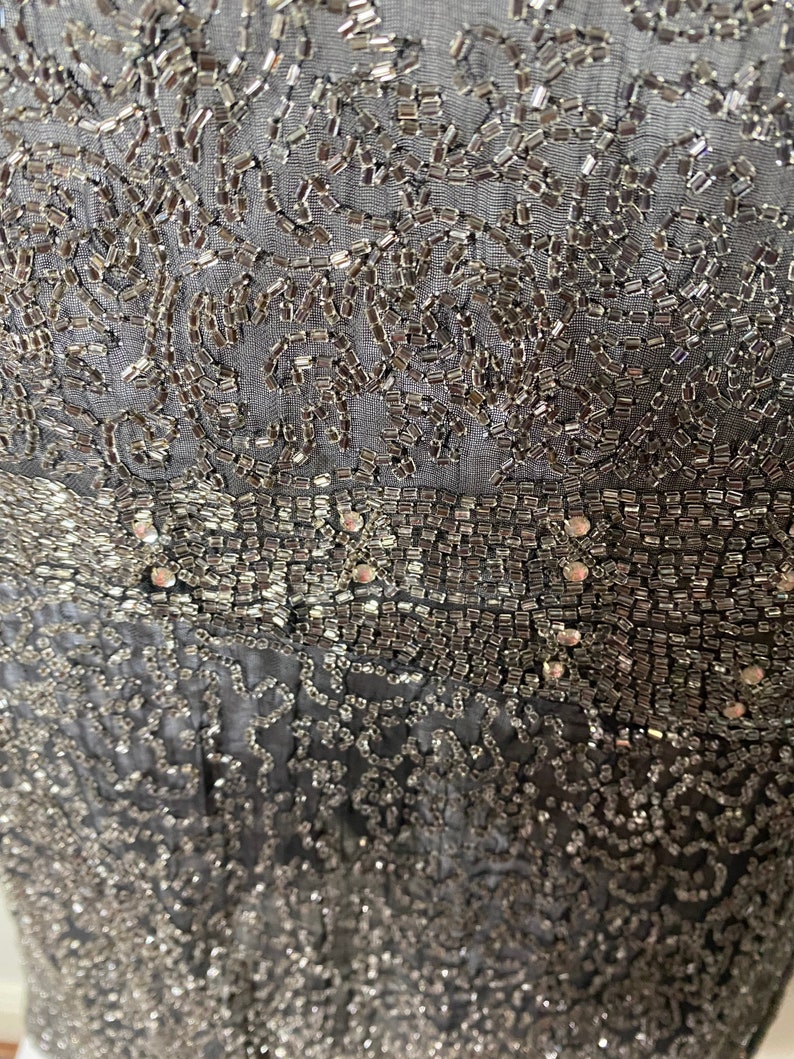 May include: A close-up of a black fabric with silver beading and sequins. The fabric has a delicate, intricate pattern.