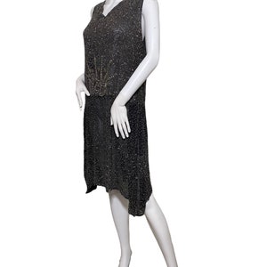 May include: A sleeveless black beaded dress with a geometric design in the center. The dress has a V-neck and a slightly asymmetrical hemline.