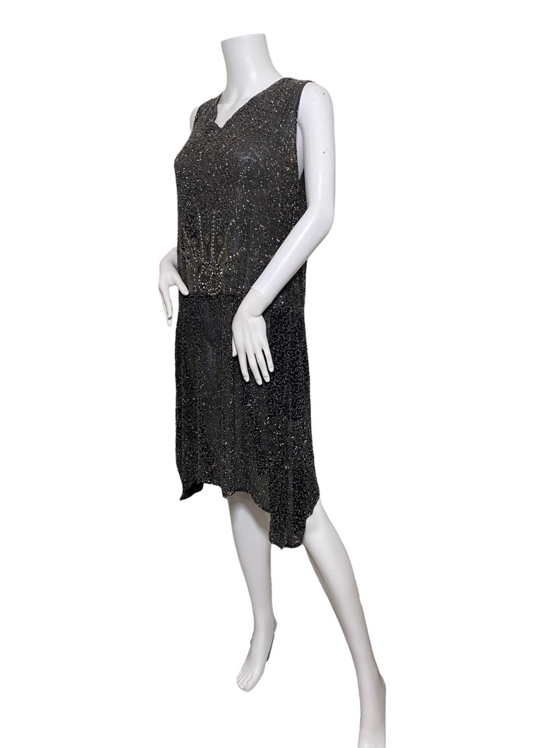 May include: A sleeveless black beaded dress with a geometric design in the center. The dress has a V-neck and a slightly asymmetrical hemline.