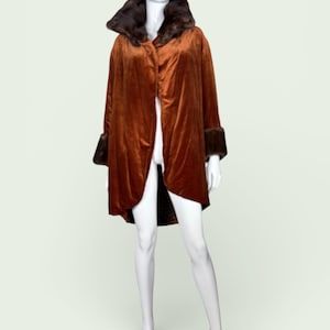 May include: A rust-coloured velvet coat with a dark brown fur collar and cuffs. The coat is displayed on a mannequin and has a flowing, open front design. The coat is a vintage style.