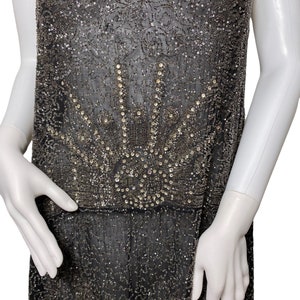 May include: A black beaded dress with a silver and crystal design. The dress has a sleeveless design and a loose fit.