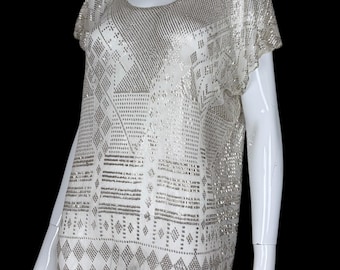 May include: A short-sleeved tunic top featuring a metallic silver and white geometric pattern. The garment has a round neckline and a loose, straight-cut silhouette with a repeating diamond and horizontal line design across the entire surface.