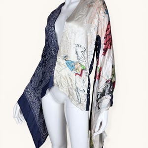 May include: A silk kimono-style jacket with a unique design. One side features a navy paisley pattern, while the other showcases a cream-colored print with equestrian and floral motifs. The jacket has wide sleeves and a flowing silhouette, perfect for layering.