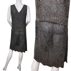 May include: A sleeveless, knee-length dress made of silver and black beads. The dress has a V-neckline and a loose, flowing silhouette.