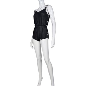 May include: A black romper featuring a sheer, lightweight fabric with a cinched elastic waist. The garment includes thin shoulder straps and side panels decorated with a repeating white and black checkered pattern along the edges and seams.