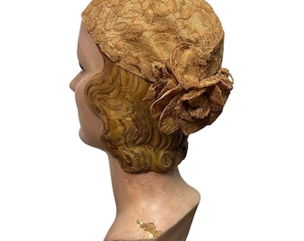 May include: A vintage brown lace hat with a large flower accent. The hat is on a mannequin head with blonde hair.