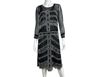 May include: A black beaded dress with a white geometric pattern. The dress has long sleeves and a knee-length skirt.