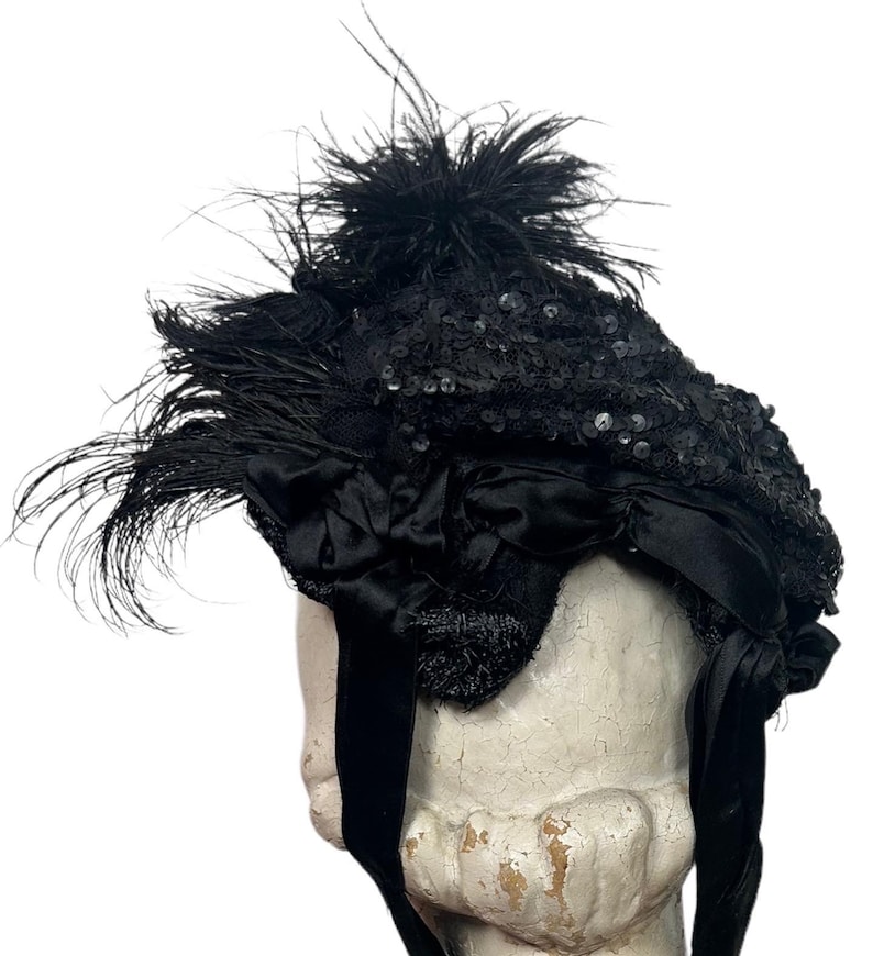 May include: A black hat with sequins, feathers, and a satin bow. The hat has a rounded crown and a wide brim. Long black ribbons hang from the hat. The hat is likely vintage or antique.