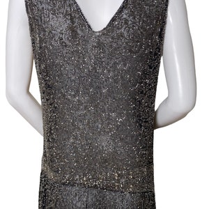 May include: A sleeveless, beaded dress in a dark gray color. The dress has a V-neckline and a beaded pattern throughout. The dress is fitted through the bodice and flows out at the hem.