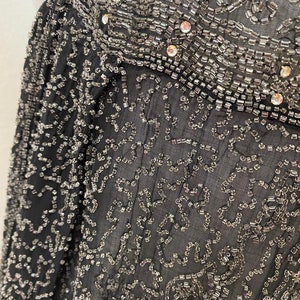 May include: Black sheer fabric with a delicate pattern of silver beads and sequins. The fabric is translucent and the beads create a shimmering effect.
