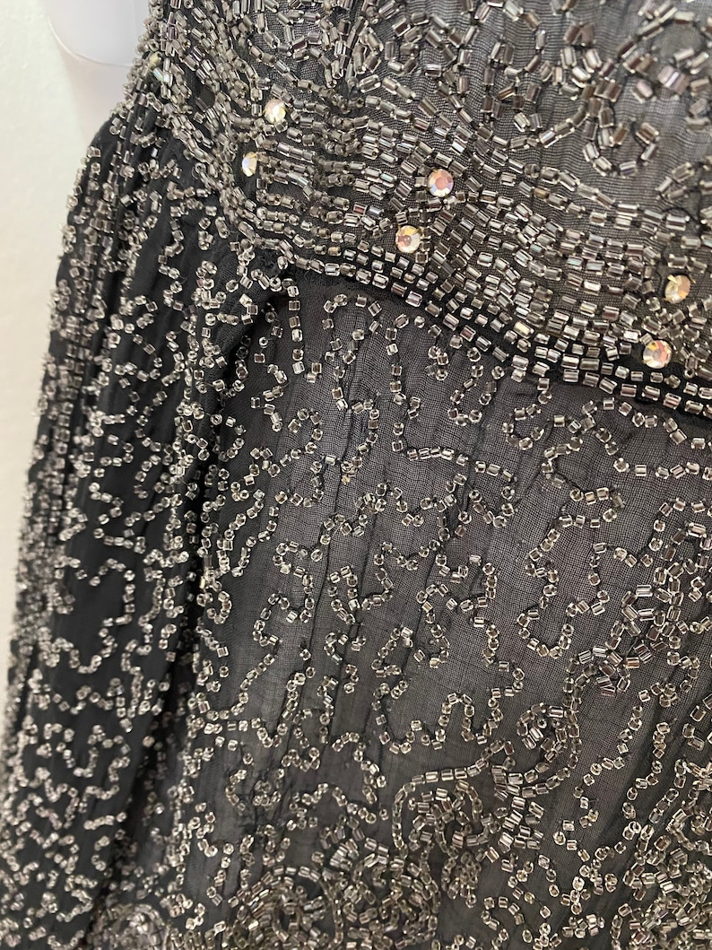 May include: Black sheer fabric with a delicate pattern of silver beads and sequins. The fabric is translucent and the beads create a shimmering effect.