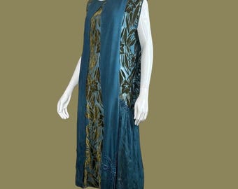 May include: A teal-colored sleeveless dress with floral patterns in shades of gold and dark green. The dress features a flowing, layered design with a pleated skirt section and delicate beadwork. The dress is displayed on a mannequin.