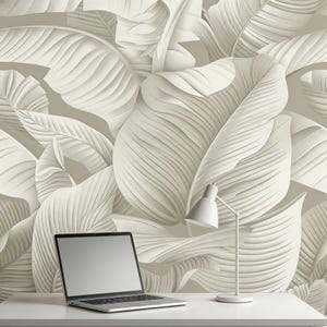 May include: A white desk with a laptop and a white desk lamp in front of a wallpaper with a repeating pattern of large, textured, off-white leaves. The leaves have prominent veining and are layered to create depth.