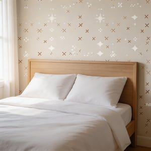May include: A bed with a light wood headboard and white bedding. The wall behind the bed is a light beige color with a pattern of white and brown star and cross shapes.