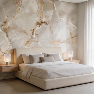May include: A modern bedroom featuring a beige upholstered bed with white bedding and several neutral-toned pillows. Two small wooden nightstands flank the bed, each with a lamp. The wall behind the bed is a large marble slab with beige and brown veining.
