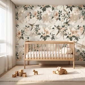 May include: A light wood baby crib with a white mattress and pillow sits on a cream-colored rug. The wall behind the crib features a floral wallpaper with birds, pink flowers, and green leaves. Wooden toy blocks, a horse, and a car are on the rug.