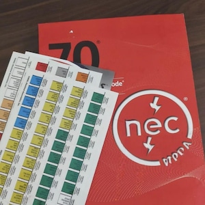 May include: A red book with the number "70" printed on the cover, along with a stack of color-coded reference cards. The book has the "nec" logo in a white circle. The cards have text and color blocks.
