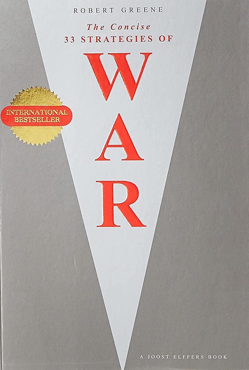May include: A book titled The Concise 33 Strategies of War by Robert Greene. The cover features a large white triangle on a gray background with the word WAR in bold red letters. A gold circular sticker reads International Bestseller.