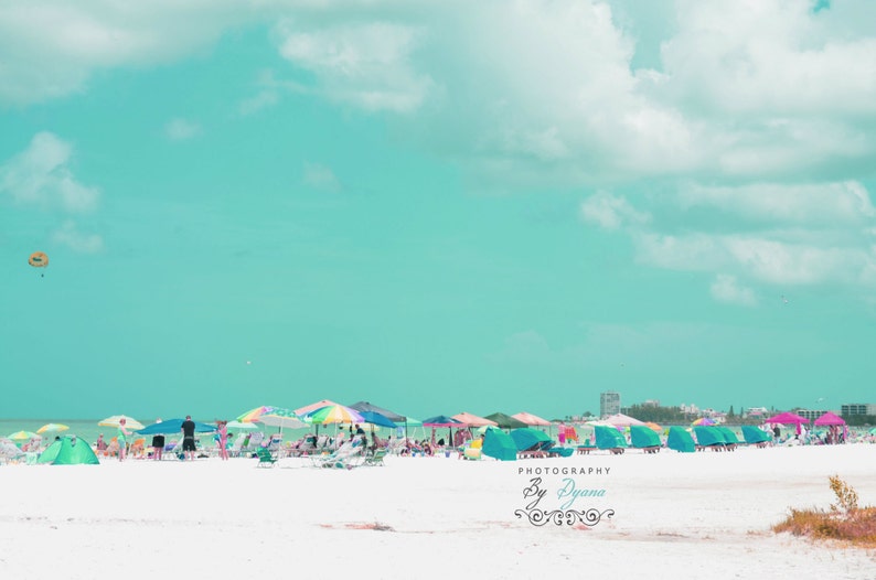 May include: A beach scene with a bright blue sky and white clouds. There are colorful umbrellas and beach chairs on the white sand beach. The text "Photography By Dyana" is in the lower right corner of the image.
