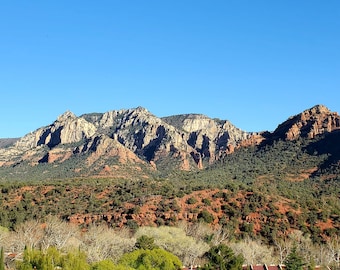 May include: A panoramic view of a mountain range with red rock formations and lush green vegetation. The sky is a clear blue.