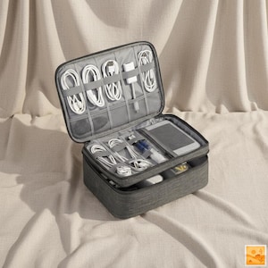 May include: Open gray travel organizer with multiple compartments filled with white charging cables, a tablet, and other electronic accessories. The case is made of a textured fabric and has a zippered closure.