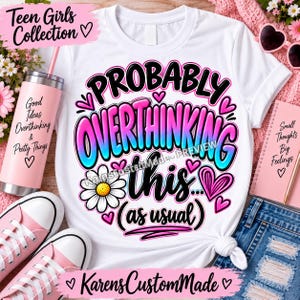 May include: A white t-shirt featuring a graphic design with the text "PROBABLY OVERTHINKING this... (as usual)" in black, pink, and blue gradient lettering, accented with pink hearts and a white daisy flower illustration.