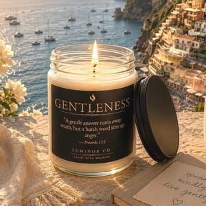 May include: A burning candle in a glass jar with a black label, the word "GENTLENESS" is visible. The candle is next to a notebook, pen, and a small cup. The background shows a coastal town and the sea.