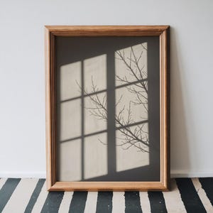 May include: A rectangular wall art piece featuring a wooden frame surrounding a print of a window pane shadow cast onto a wall, with the dark silhouette of bare tree branches extending across the light-colored rectangular window light shapes.