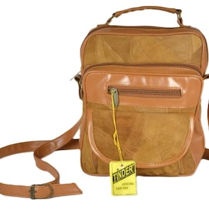 Peut inclure: Un sac à bandoulière en cuir patchwork marron et beige avec une poignée supérieure et une sangle réglable. Le sac présente une poche avant zippée, une fermeture à rabat et une étiquette jaune attachée à la tirette indiquant TINDER GENUINE LEATHER.