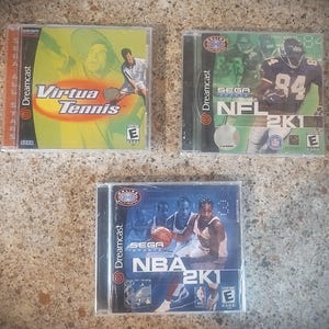 May include: Three Sega Dreamcast video game cases including Virtua Tennis with a yellow background, NFL 2K1 featuring a football player in a dark jersey, and NBA 2K1 showing a basketball player dribbling a ball on a blue background.