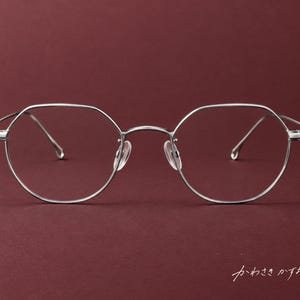 May include: Silver-toned metal eyeglasses featuring a distinct hexagonal frame shape, thin temples, and clear nose pads. The lower right corner of the image displays the Japanese text "かわさきかずお" in a white, cursive script font.