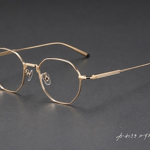 May include: Gold-toned metal spectacles featuring an octagonal frame shape, thin temples with a ribbed texture, and clear lenses. The bottom right corner of the image displays the Japanese text "かわさきかずお".