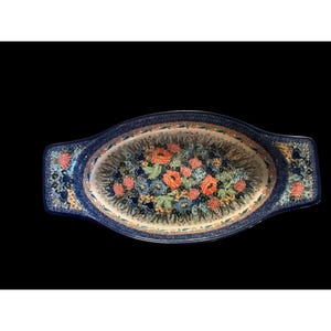 Könnte beinhalten: Eine ovale Auflaufform aus Keramik mit integrierten Griffen, die einen dunkelblauen Rand und ein zentrales Blumenmuster aus orangefarbenen, blauen und rosa Blüten mit grünem Laub auf cremefarbenem Grund sowie einen gesprenkelten blauen Rand aufweist.