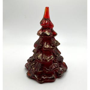 May include: A decorative glass tree figurine in a deep red hue, featuring a tiered, conical shape with textured branches. The surface of the glass is accented with shimmering gold-coloured flecks embedded throughout the structure, creating a reflective and layered appearance from the base to the pointed top.