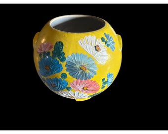 Peut inclure: Un cache-pot rond en céramique jaune orné d'un motif floral peint à la main avec des pétales texturés dans des tons de blanc, bleu clair et rose. Le récipient présente une large ouverture circulaire, une finition lisse et brillante.